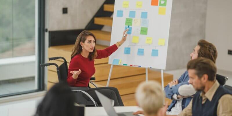 Smart business woman sitting in a wheelchair, points to a process chart in a business meeting,